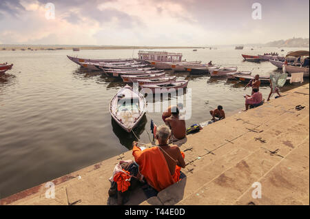 Varanasi Ganges River Bank mit Blick auf die Boote aus Holz und sadhu Baba sitzen auf der Treppe. Stockfoto