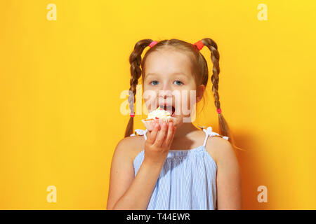 Closeup Portrait von ein fröhliches kleines Mädchen auf einem gelben Hintergrund. Ein Kind mit Flechten der Haare bissen Kuchen. Stockfoto