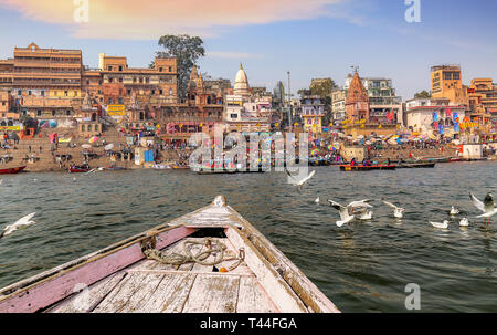 Varanasi alten Indien Stadt Architektur auf, die von einem Boot auf dem Fluss Ganges mit Blick auf Zugvögel mit stimmungsvollen Sonnenuntergang Himmel gesehen Stockfoto