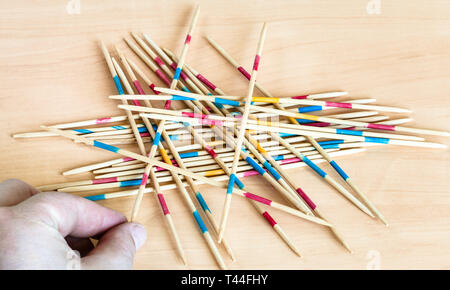 Spieler nimmt einen Stick von Stapel in Mikado pick-up sticks Spiel auf Holzbrett Stockfoto