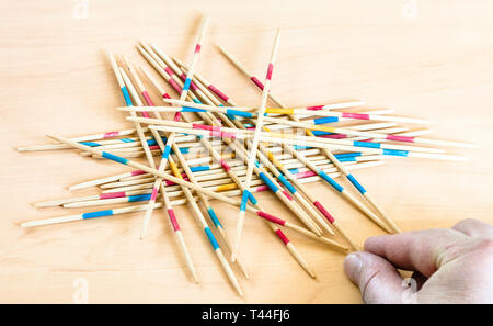 Spieler nimmt einen Stick von Stapel in Mikado Spiel auf Holzbrett Stockfoto