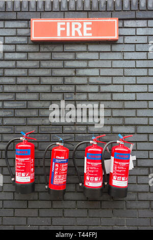 Eine Reihe von vier an der Wand montierten roten Chubb portable trockenes Pulver Feuerlöscher gegen eine graue Mauer gesetzt Stockfoto