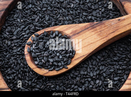 Schwarze Sesamsamen in der Löffel aus Holz. Sesamsamen in die Schüssel im Hintergrund. Ansicht von oben. Stockfoto