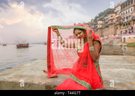 Junge indische Mädchen in traditioneller Kleidung (Sari) posieren für ein Foto mit Blick auf die historische Architektur und Stadt Varanasi Ganges Ghat in der Dämmerung. Stockfoto