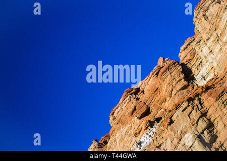 Orangefarbene Felswand in der Wüste unter einem strahlend blauen Himmel. Stockfoto