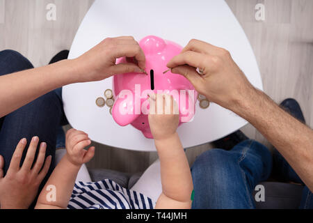 Erhöhten Blick auf Familie, Münze in Sparschwein auf dem Tisch Stockfoto