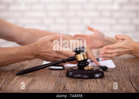 In der Nähe von Paar streiten Miteinander und Schlägel mit goldenen Ringen auf hölzernen Schreibtisch Stockfoto