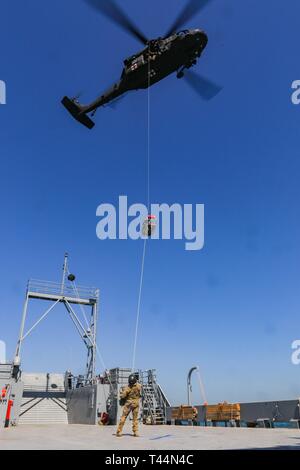 Us-Armee Soldaten zu C., 2. Bataillon, 211 Allgemeine Unterstützung Aviation Battalion, Minnesota Army National Guard zugewiesen, ein Korb hoist in eine UH-60L Black Hawk Hubschrauber an Bord des Landing Craft, Utility 2027, USAV Mechanicsville, in den Persischen Golf in der Nähe von der Kuwait Naval Base, Feb 20, 2019. C. in der Firma durchgeführt Aeromedical evacuation Hebezeuge von LCU 2027 Wetter Deck Crew Mitglieder mit einem Hebezeug das Verfahren über eine verankert und bewegten Schiffes vertraut zu machen. Stockfoto