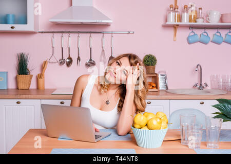 Besorgt und traurig Student weiblich Suche von Informationen in einem Laptop online in der Küche sitzt. Traurig blonde Frau Stress wegen der finanziellen Stockfoto