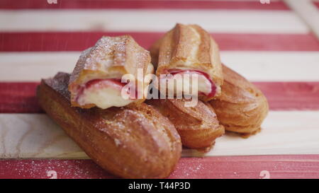 Frische gesichert eclairs Cookies liegen auf einem rot-weiß gestreiften Holz- Fach und zur Besprengung mit Zucker Pulver in 4 K Zeitlupe mittellange Aufnahme video Stockfoto