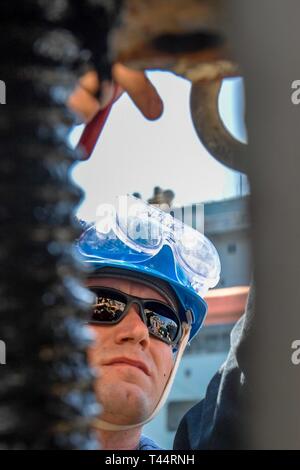 ARABIAN GULF (Feb. 21, 2019) der Bootsmann Mate 2. Klasse Jason Myers bereitet Takelage an Bord der Arleigh-Burke-Klasse geführte Anti-raketen-Zerstörer USS Mitscher (DDG57) während einer Auffüllung-auf-See mit der Lewis und Clark-Klasse Dry Cargo und Munition ship USNS Alan Shepard (T-AKE 3). Mitscher ist in die USA 5 Flotte Bereich der Maßnahmen zur Unterstützung der Marine im Einsatz für die Stabilität und Sicherheit in der Region zu gewährleisten und verbindet das Mittelmeer und den Pazifischen Raum durch den westlichen Indischen Ozean und drei strategischen Punkten ersticken. Stockfoto