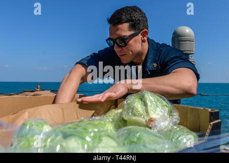 ARABIAN GULF (Feb. 21, 2019) Chief Hospital Corpsman Mario Zavala prüft entgegenkommenden produzieren an Bord der Arleigh-Burke-Klasse geführte Anti-raketen-Zerstörer USS Mitscher (DDG57) während einer Auffüllung-auf-See mit der Lewis und Clark-Klasse Dry Cargo und Munition ship USNS Alan Shepard (T-AKE 3). Mitscher ist in die USA 5 Flotte Bereich der Maßnahmen zur Unterstützung der Marine im Einsatz für die Stabilität und Sicherheit in der Region zu gewährleisten und verbindet das Mittelmeer und den Pazifischen Raum durch den westlichen Indischen Ozean und drei strategischen Punkten ersticken. Stockfoto