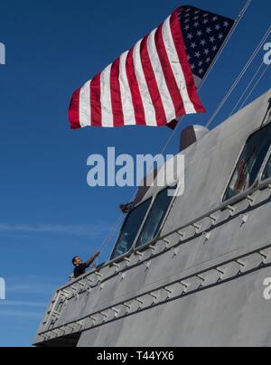 CHARLESTON, SOUTH CAROLINA (Feb. 25, 2019) Chief Quartermaster Johnathan Restrepo, aus Cali, Kolumbien, senkt die nationalen Fähnrich an Bord der USS Charleston (LCS 18) als die Besatzung des Littoral Combat Ship bereitet sich auf die bevorstehende Inbetriebnahme Zeremonie. Charleston wird dem 16 Littoral Combat Ship, der Flotte und der 9. Unabhängigkeit Variante eingeben. Es ist auch das sechste Schiff namens für Charleston, die älteste und größte Stadt im US-Bundesstaat South Carolina. Stockfoto