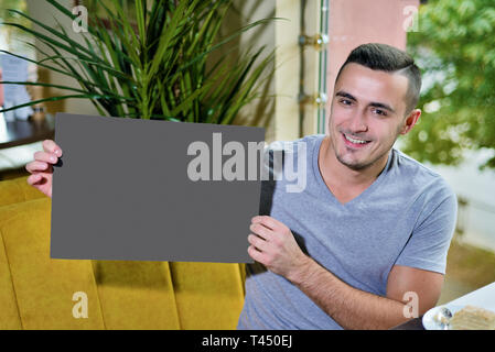 Porträt der jungen Kerl in Cafe. Mann hält in seinen Händen eine leere Tabelle kopieren Platz für Text. Stockfoto