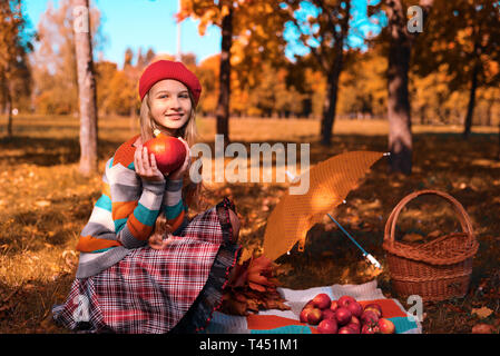 Herbst Porträt einer schönen jungen Mädchen in einem Red Hat. teenager hält eine reife Kürbis und lächelt. Äpfel sind auf der Tagesdecke. yellow umbrella und wic Stockfoto