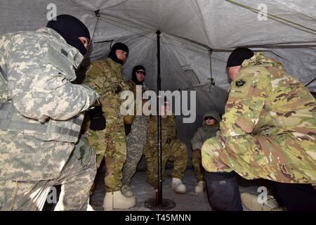 Staff Sgt. Andreas Janka, nördlichen Warfare Training Center Instructor, Gespräche mit Mitgliedern seiner kalten Wetter Führer Kurs 19-004 Squad in der Arktis 10-Mann Zelt am Schwarzen Rapids Training Website März 2 Die Nördliche Warfare Training Center, 2019. Das kalte Wetter Führer Kurs schult Kader- und platoon-Führer in die Kenntnisse und Fähigkeiten, die zur erfolgreichen kleinen unit operations in einer kalten, verschneiten Umgebung durchführen. Schwerpunkt liegt dabei auf den Auswirkungen der Kälte auf Personal und Material, die Nutzung von grundlegenden kaltem Wetter Kleidung und Ausrüstung, winter Bereich Handwerk, Schneeschuh und Ski te Stockfoto