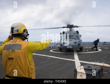 Philippinischen MEER (10. März 2019) der Bootsmann Mate 3. Klasse Exavien Alvarado Signale an einen Seemann, als er bewegt sich weg von einer SH-60S Seahawk Hubschrauber, der "Insel der Ritter" Hubschrauber Meer Combat Squadron 25 (HSC 25), nach der Befestigung an der Flight Deck der Arleigh-Burke-Klasse geführte Anti-raketen-Zerstörer USS Curtis Wilbur (DDG54) während des Betriebs im philippinischen Meer. U.S. Navy Kriegsschiffe Zug zusammen die taktischen Kenntnisse, Letalität zu erhöhen und die Interoperabilität der teilnehmenden Einheiten in einer Zeit, in der Große-Wettbewerb. Stockfoto