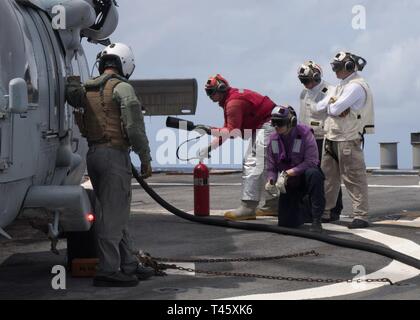 Philippinischen MEER (10. März 2019) Segler tanken ein SH-60S Seahawk Hubschrauber, der "Insel der Ritter" Hubschrauber Meer Combat Squadron 25 (HSC 25), auf dem Flugdeck der Arleigh-Burke-Klasse geführte Anti-raketen-Zerstörer USS Curtis Wilbur (DDG54) während des Betriebs im philippinischen Meer. U.S. Navy Kriegsschiffe Zug zusammen die taktischen Kenntnisse, Letalität zu erhöhen und die Interoperabilität der teilnehmenden Einheiten in einer Zeit, in der Große-Wettbewerb. Stockfoto