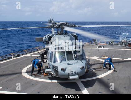 Philippinischen MEER (10. März 2019) Segler mit Unterlegkeilen sichern und die Kette ein SH-60S Seahawk Hubschrauber, der "Insel der Ritter" Hubschrauber Meer Combat Squadron 25 (HSC 25), auf dem Flugdeck der Arleigh-Burke-Klasse geführte Anti-raketen-Zerstörer USS Curtis Wilbur (DDG54) während des Betriebs im philippinischen Meer. U.S. Navy Kriegsschiffe Zug zusammen die taktischen Kenntnisse, Letalität zu erhöhen und die Interoperabilität der teilnehmenden Einheiten in einer Zeit, in der Große-Wettbewerb. Stockfoto