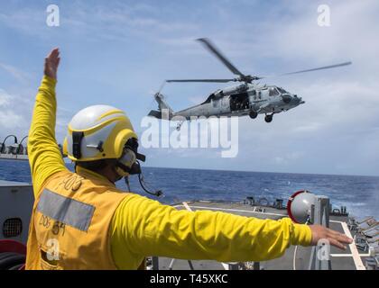 Philippinischen MEER (10. März 2019) der Bootsmann Mate 3. Klasse Exavien Alvarado Signale an ein SH-60S Seahawk Hubschrauber, der "Insel der Ritter" Hubschrauber Meer Combat Squadron 25 (HSC 25), er fährt das Flight Deck der Arleigh-Burke-Klasse geführte Anti-raketen-Zerstörer USS Curtis Wilbur (DDG54) während des Betriebs im philippinischen Meer. U.S. Navy Kriegsschiffe Zug zusammen die taktischen Kenntnisse, Letalität zu erhöhen und die Interoperabilität der teilnehmenden Einheiten in einer Zeit, in der Große-Wettbewerb. Stockfoto