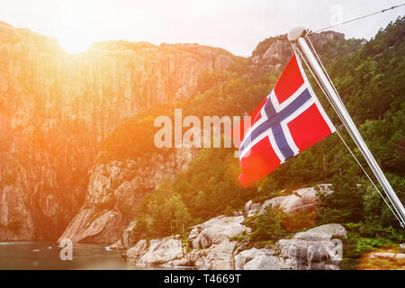 Norwegische Flagge auf dem Fjord, umgeben von Bergen. Sonniges Wetter. Tourismus, touristische Destination. Stockfoto