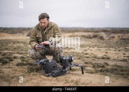 Lettische Armee Staff Sgt. Gatis Indrevics, eine Bekämpfung der Kameramann mit der lettischen Armee, bereitet eine Drohne vor einem US Marine Corps High Mobility Artillery Rocket System live - Feuer bei Adazi, Lettland, 4. März 2019, während der übung Dynamische Front 19. Zwei HIMARS von Fox. Akku, 2. Bataillon, 14 Marine Regiment, 4 Marine Division, Brände mit Armee Einheiten in Deutschland koordiniert. Rund 3.200 Teilnehmer aus 27 Nationen werden an der live-fire Teil der Übung Dynamische Front 19, March 2-9, 2019, in der US-Armee Grafenwöhr Training Area, Deutschland; sowie in Stockfoto