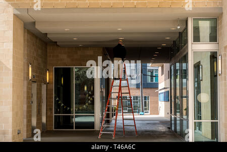 Arbeiter auf Leiter ändern Glühbirne außerhalb kommerzieller Gebäude Stockfoto