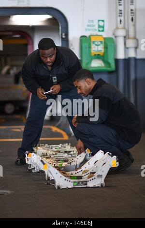 Pazifik (XX März 2019) Aviation Maintenance Administrationman 2. Klasse Lowell Wilson, von Woodbridge, Virginia, Links, und Aviation Ordnanceman Airman Brian Bellamy, von Baton Rouge, La., rechts, Seriennummern Prüfen auf Bombe Adapter für Munition Transporter in den Hangar Bucht der Flugzeugträger USS Theodore Roosevelt (CVN 71). Theodore Roosevelt ist die Durchführung von Routineaufgaben im östlichen Pazifik. Stockfoto