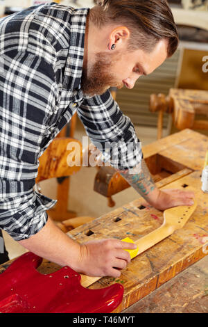 Nahaufnahme des Handwerkers Schleifen einen Gitarrenhals aus Holz in Werkstatt Stockfoto