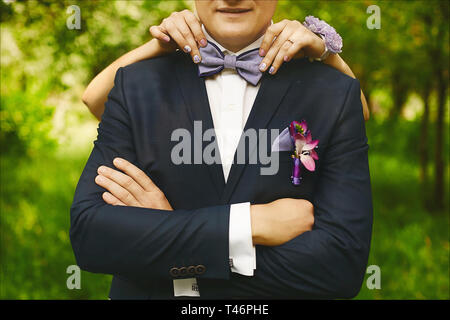 Weibliche Hände mit modischen Maniküre einstellen trendy bowtie auf dem Hals eines jungen gutaussehenden Mann in einer Hochzeit Anzug mit Anstecker Stockfoto