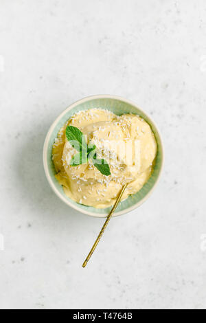 Hausgemachte veganes Eis in eine Schüssel aus Gefrorenes Mango und Kokosmilch von frischer Minze und Flocken auf einem weißen Tisch serviert. Stockfoto
