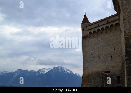 Mittelalterlichen Turm und Mauer des Schloss Chillon, Montreux, Schweiz, an einem bewölkten Tag im Frühjahr (April) am Genfer See gegen die schneebedeckten Berge im Hintergrund Stockfoto