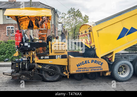 Presteigne, Powys, Wales, UK. Ein fertiger Asphalt oder Pflaster Maschine mit frischem Asphalt auf einer Straße in der Stadt, als Kipper nachgefüllt werden Stockfoto