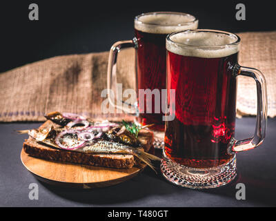 Red Handwerk Bier, heiß geräucherter Fisch Sandwich auf einem dunklen Hintergrund. Low Key Beleuchtung. Stockfoto