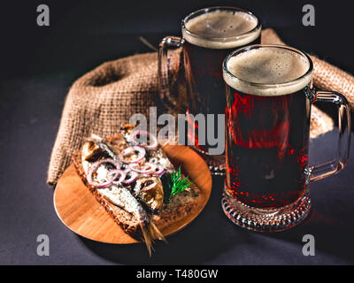 Red Handwerk Bier, heiß geräucherter Fisch Sandwich auf einem dunklen Hintergrund. Low Key Beleuchtung. Stockfoto