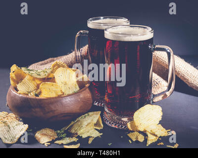 Red Handwerk Bier und Chips in eine hölzerne Schüssel auf einem dunklen Hintergrund. Low Key Beleuchtung. Stockfoto