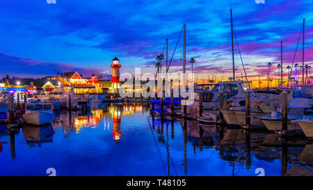 Oceanside Harbor kurz nach Sonnenuntergang mit Leuchtturm und Wharf beleuchtet, Lichter reflektiert das blaue Wasser und die Boote angedockt. Bunte Himmel. Stockfoto