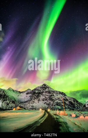 Aurora Borealis (Nordlicht) Explosion über Berge und ländliche Straße bei Skagsanden Strand, Lofoten Inseln, Norwegen Stockfoto