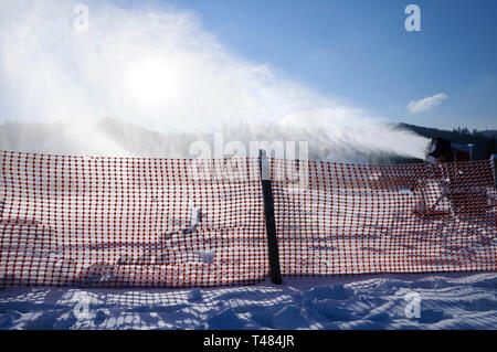 Landschaft von einem Berg, Skigebiet Pisten als Hintergrund für Zaun und Beschneiungsanlage mit weißem Pulver in der Luft - künstlichen Schnee. Winterurlaub Stockfoto