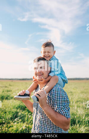 Mann, der Junge piggyback Ride im Freien lächelnd. Vater verbringt Zeit mit seinem Sohn. Stockfoto