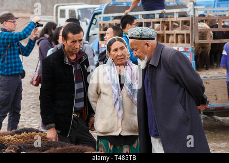 Gespräch zwischen einer älteren Frau und einem Älteren, bärtigen Mann trägt einen doppa am Kashgar Tiermarkt (Provinz Xinjiang, China) Stockfoto