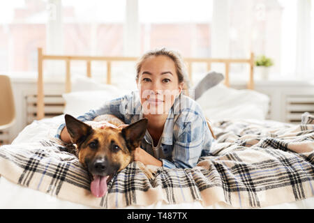 Junge asiatische Frau posiert mit Hund auf dem Bett Stockfoto