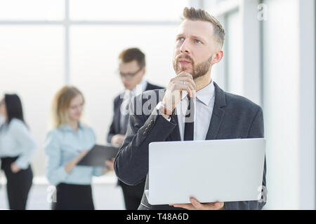 Nachdenklich Geschäftsmann mit Laptop steht im Flur des Amtes. Mensch und Technik Stockfoto