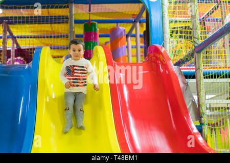 Little Boy geht eine Rutsche auf dem Spielplatz. Er lacht und Spaß auf dem Jungle Gym. Junge Reiter aus Kinder rutschen auf dem Spielplatz. Stockfoto