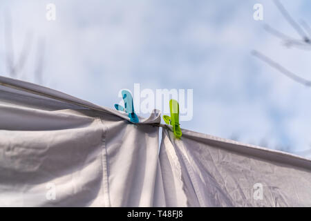 Weiße Kleidung hingen auf einer Wäscheleine zum Trocknen und durch die Kleidung befestigt Pflöcke gegen den blauen Himmel im hellen warmen sonnigen Tag Stockfoto