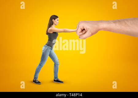 Junge brünette Mädchen mit lässigen Jeans und T-Shirt, stop Geste gegenüber großen männlichen gedehnt Faust auf gelbem Hintergrund Stockfoto