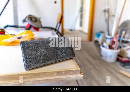 Graue grober Sand Papier mit Griff Inhaber auf eine Tabelle in einem Arbeitsraum Closeup konzentrierte sich mit anderen Arbeiten, Werkzeuge, Geräte und Gegenstände im Hintergrund Stockfoto