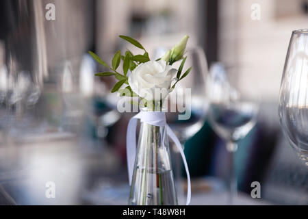 Transparentes Glas Vase mit Blumenstrauß vor Hintergrund der Tabelle Einstellung im modernen Restaurant. Wein und Wasser Gläser stehen in der Zeile auf Holz Stockfoto