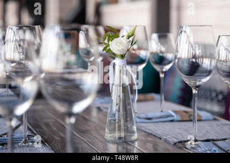 Transparentes Glas Vase mit Blumenstrauß vor Hintergrund der Tabelle Einstellung im modernen Restaurant. Wein und Wasser Gläser stehen in der Zeile auf Holz Stockfoto