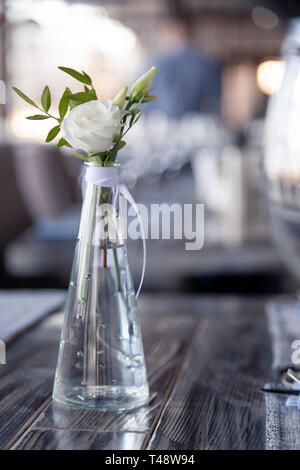 Transparentes Glas Vase mit Blumenstrauß vor Hintergrund der Tabelle Einstellung im modernen Restaurant. Wein und Wasser Gläser stehen in der Zeile auf Holz Stockfoto